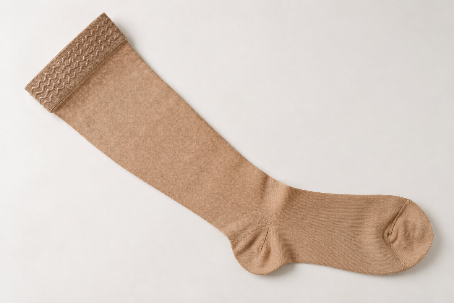 Une longue chaussette beige est étendue en diagonale sur un fond blanc.